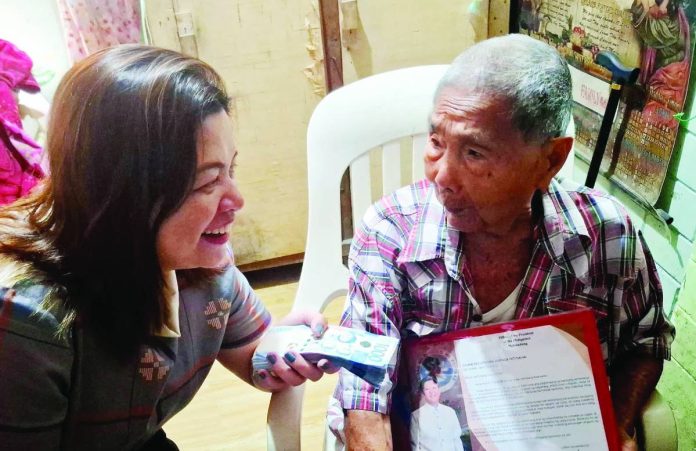 MILESTONE GIFT. National Commission of Senior Citizens’ Western Visayas director Ann Rapunzel Ganzon shares a light moment with centenarian Lolo Resurreccion Tacusalme of Barangay San Isidro, Jaro, Iloilo City, as she personally hands him his ₱100,000 cash gift and presidential letter of felicitation under the Expanded Centenarians Act. NCSC-6 PHOTO