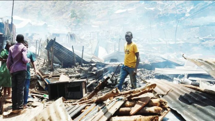 Congo A man stands in piles of rubble and corrugated iron left by a school fire in he Democratic Republic of Congo while three other people stand on the left of the picture. The rubble seems to go on for some distance and the air is hazy. REUTERS