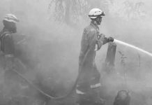 Two firefighters in bright orange uniform and helmets, standing outdoors in thick white haze, spray water from a hose in Indonesia. GETTY IMAGES