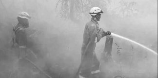 Two firefighters in bright orange uniform and helmets, standing outdoors in thick white haze, spray water from a hose in Indonesia. GETTY IMAGES