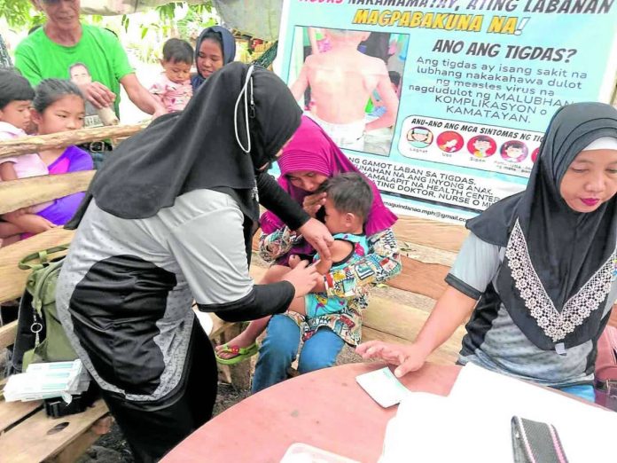 A barangay health worker gives a boy his measles vaccine shot as part of the government’s mass vaccination campaign in the Bangsamoro Autonomous Region in Muslim Mindanao. PHOTO COURTESY OF RURAL HEALTH UNIT PAGALUNGAN