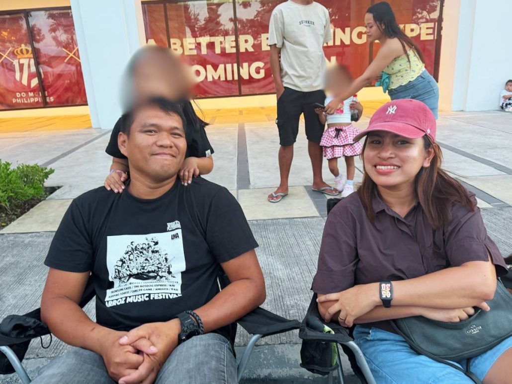 Audi Johnson and his family sit in foldable chairs at Megaworld’s The Upper East, the starting point of the MassKara Electric Float Parade, as they await its opening on Oct. 16, 2026.