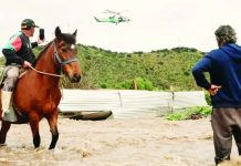A man on a horse takes a video of a helicopter hovering overhead. Another man stands nearby, with the water reaches his knees. The Mapocho river in central Chile burst its banks after heavy rains. JAVIER TORRES/EPA/SHUTTERSTOCK