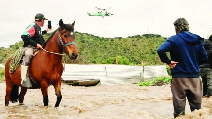 Chile_copy_compressed_resized A man on a horse takes a video of a helicopter hovering overhead. Another man stands nearby, with the water reaches his knees. The Mapocho river in central Chile burst its banks after heavy rains. JAVIER TORRES/EPA/SHUTTERSTOCK