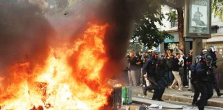 A large fire burns on a road in Paris beside which five officers in riot gear walk past a crowd observing the flames. Hundreds of thousands of protesters take to the streets across France. REUTERS