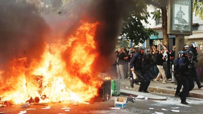 France A large fire burns on a road in Paris beside which five officers in riot gear walk past a crowd observing the flames. Hundreds of thousands of protesters take to the streets across France. REUTERS