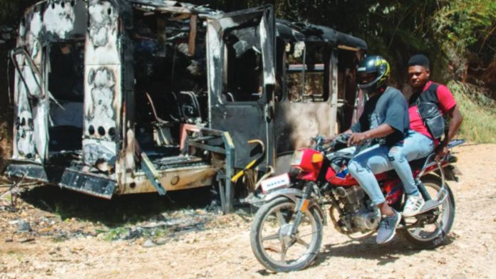 Haiti Two men on a motorbike, both wearing t-shirts and jeans, ride past a burned out motor home parked on a rural road in Haiti. The United Nations say hundreds of casualties were caught in the crossfire during security operations clamping down on gang violence. EPA