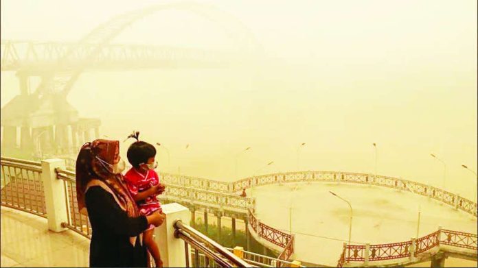 A mother and her child wearing facemasks look on from a bridge as thick haze from forest and land fires block their view of a region in Palangkaraya, Central Kalimantan, Indonesia. Persistent haze this year has prompted Indonesian authorities to step up efforts to punish offenders. GETTY IMAGES