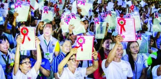 Agrarian reform beneficiaries raise their newly awarded land titles during the Department of Agrarian Reform (DAR) – Region 6’s mass distribution ceremony at the Iloilo National High School in La Paz, Iloilo City. DAR distributed 11,965 e-titles covering 18,598 hectares to 10,998 farmers across Panay and Guimaras islands, strengthening individual land ownership and tenure security among beneficiaries. ALLEN ANIMAS/PN