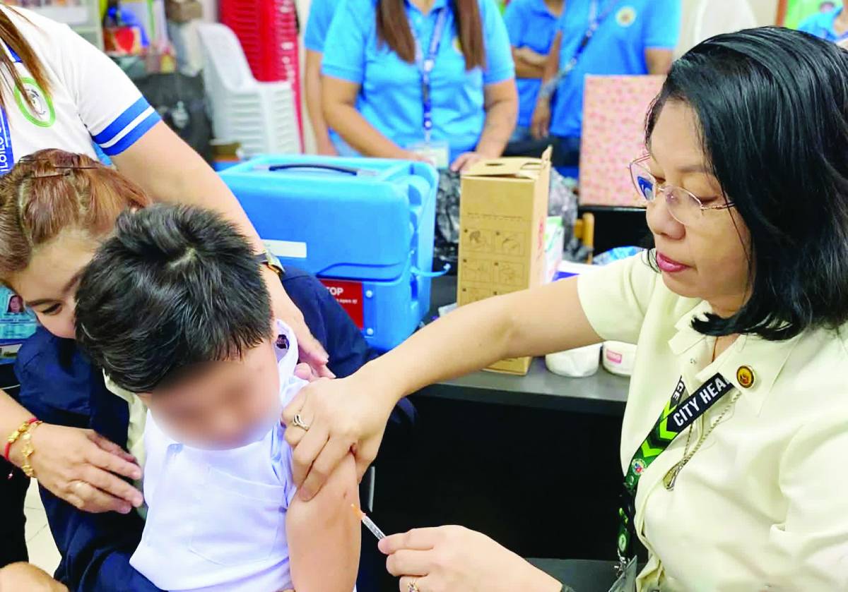 Health workers inoculate children during a school-based immunization drive in Iloilo City. The CHO is mounting an expanded